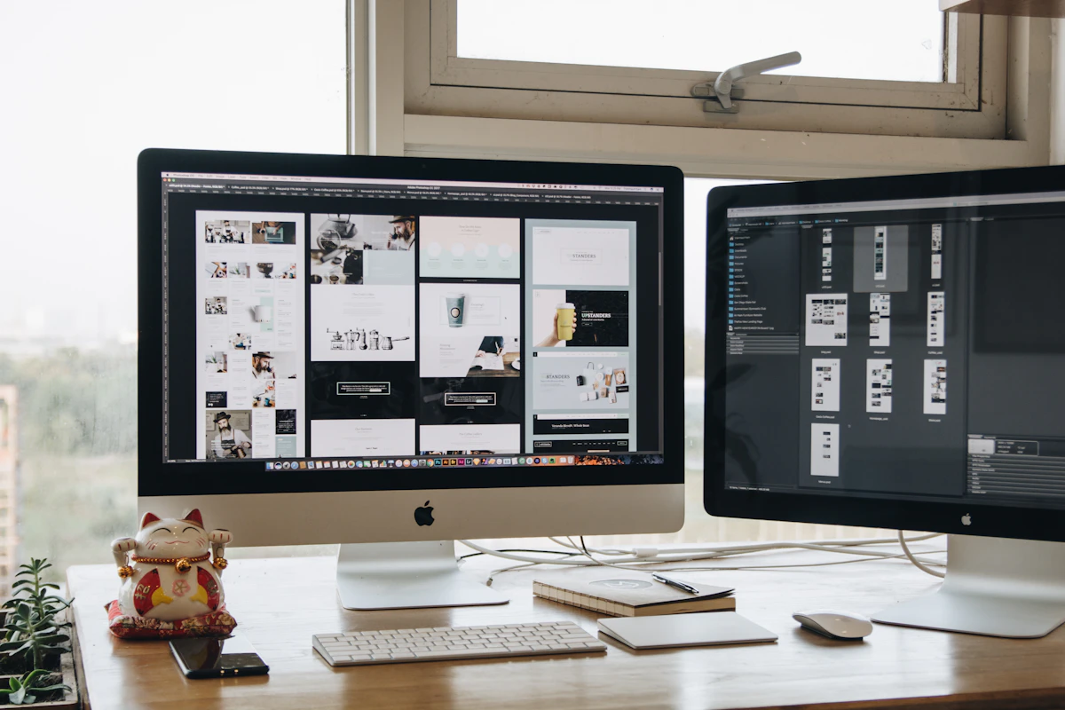Secretária de designer com dois monitores a mostrar layouts de sites