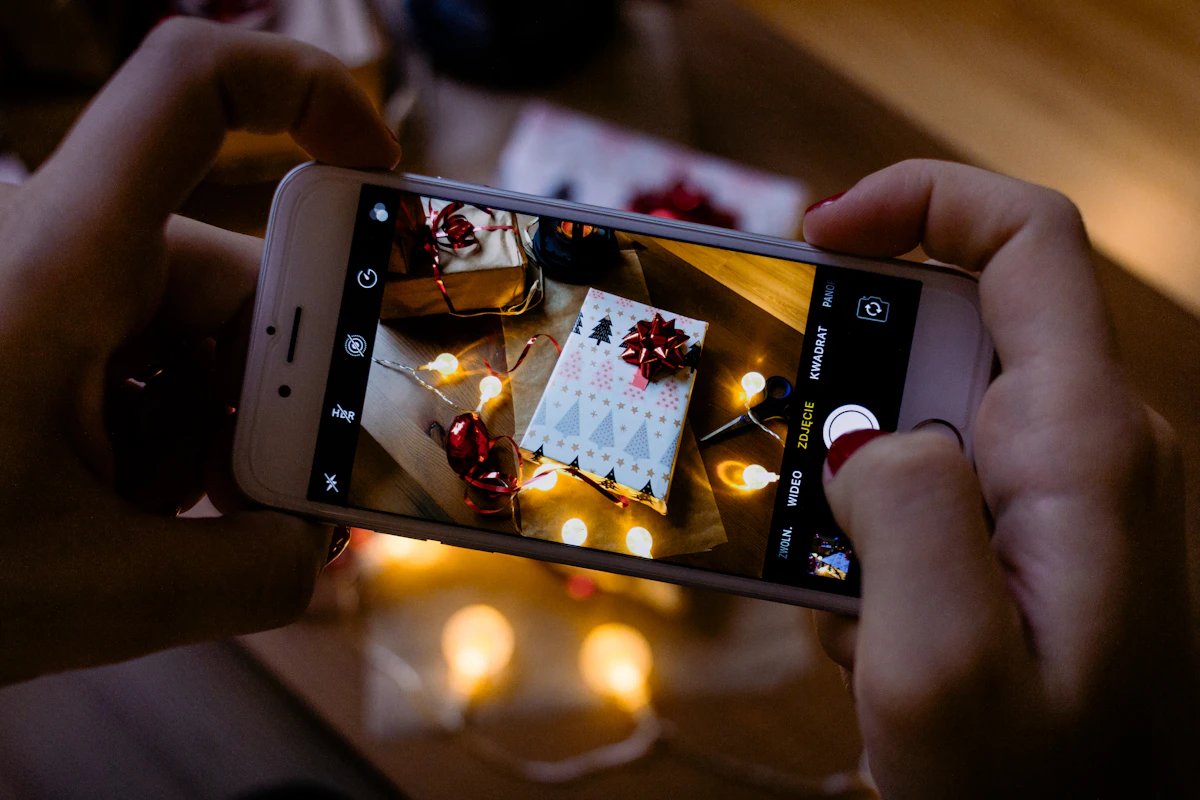 Mãos a fotografar com o telemóvel um presente embrulhado junto a luzes de Natal