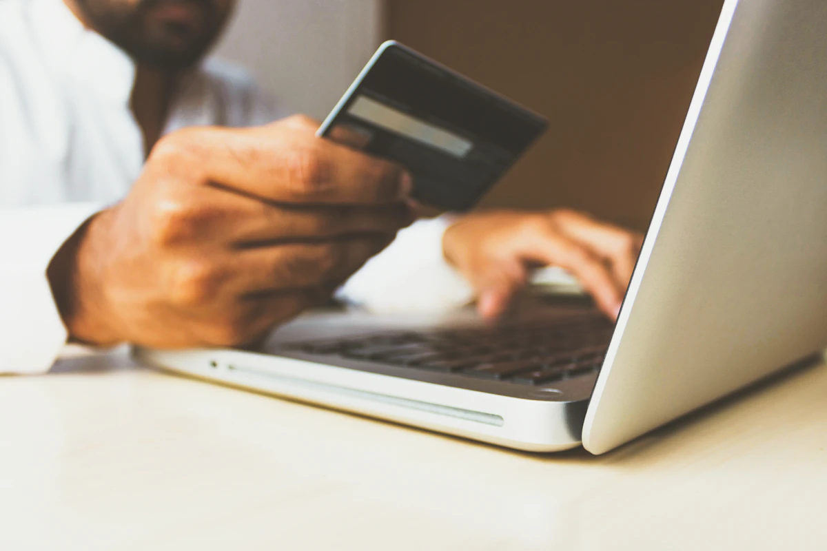 Pessoa a segurar um cartão bancário enquanto usa um portátil para comprar online