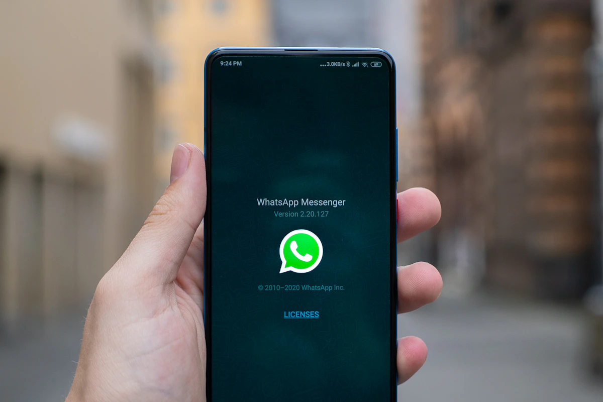 Mão a segurar um telemóvel a abrir o WhatsApp, numa rua