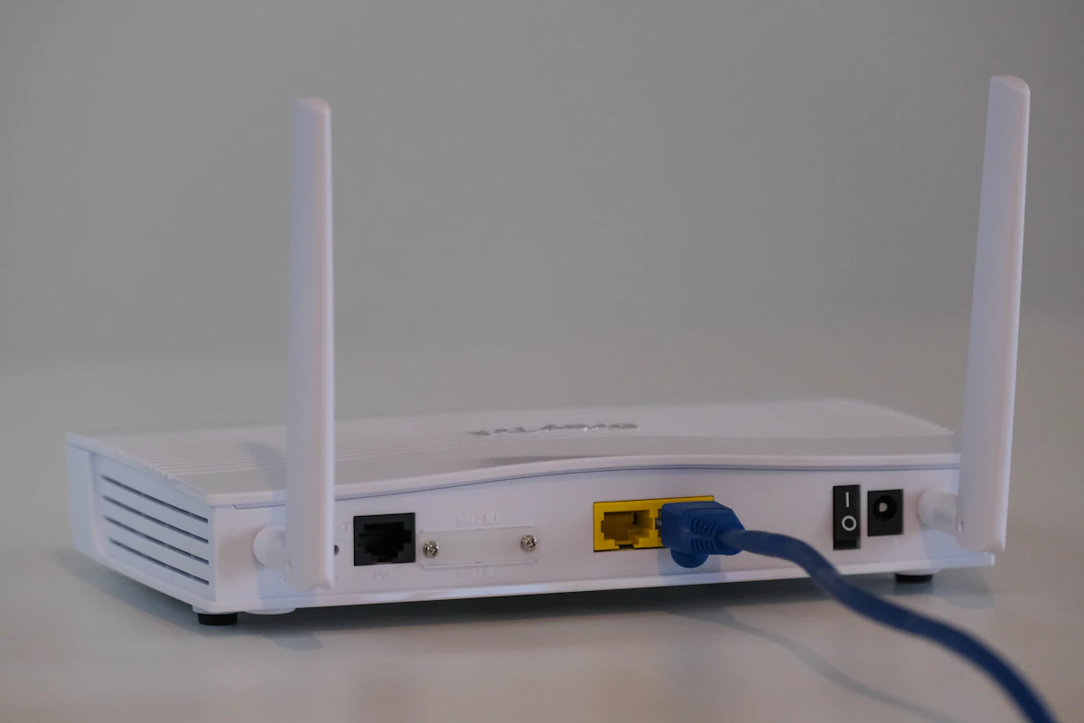 Router branco com duas antenas e um cabo de rede azul ligado, numa mesa branca