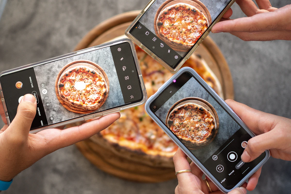 Várias mãos a fotografar com telemóveis uma pizza acabada de sair do forno, numa mesa