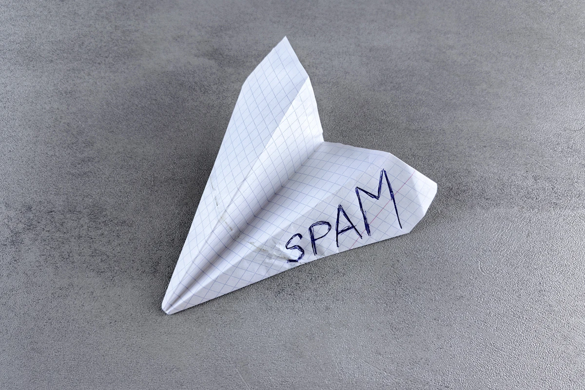 Avião de papel com a palavra SPAM escrita à mão, pousado numa superfície cinzenta