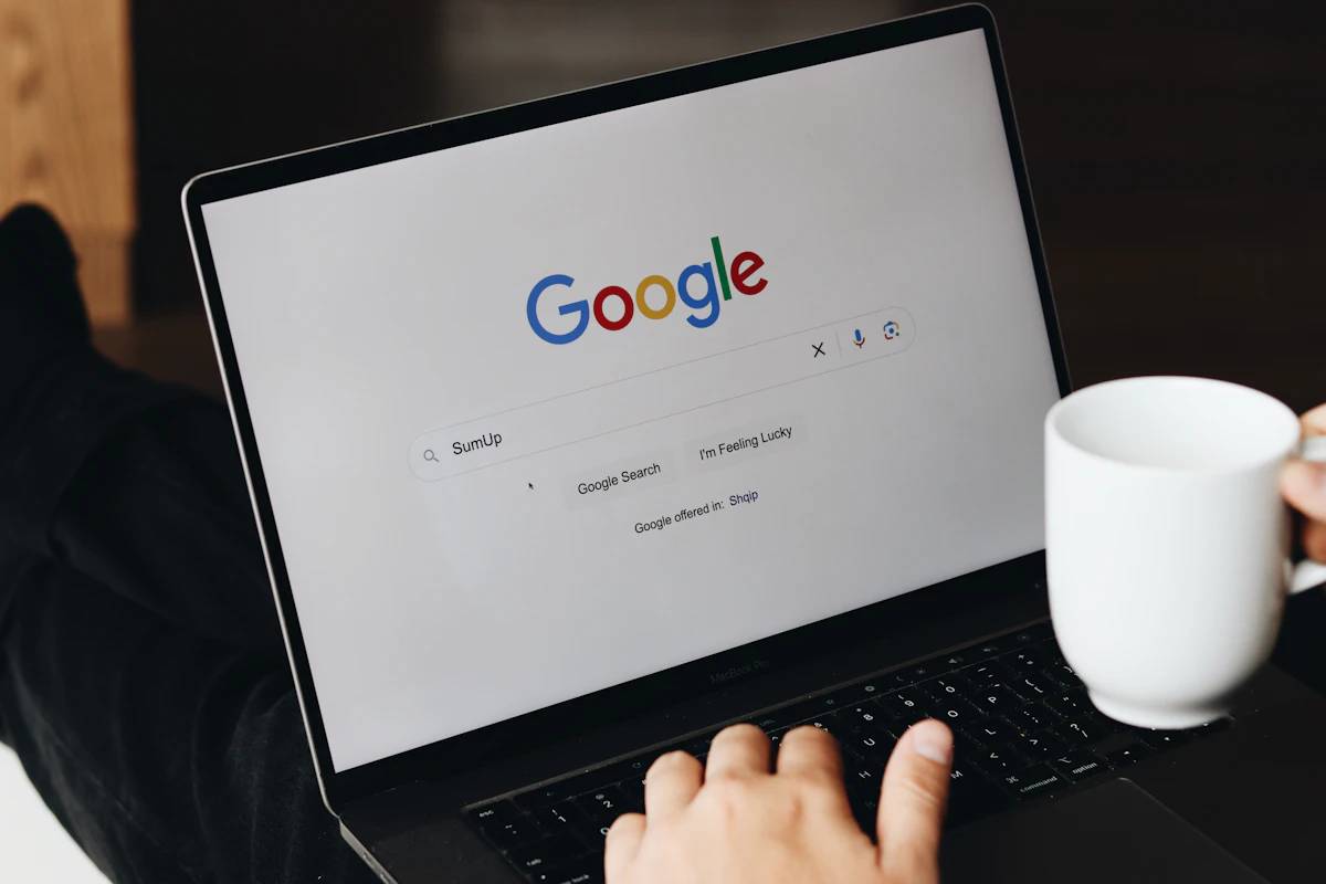 Mãos num portátil com a página de pesquisa da Google aberta, ao lado de uma caneca branca