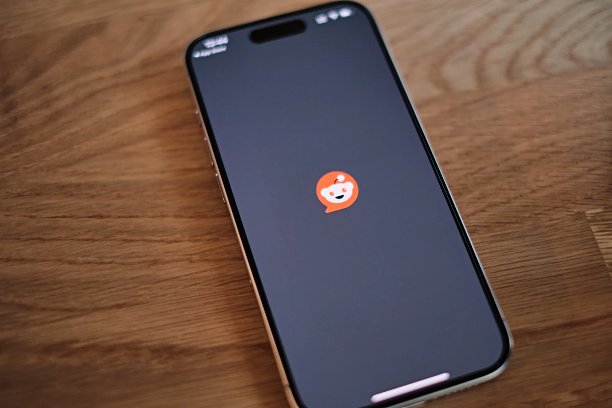 Telemóvel pousado numa mesa de madeira com o logótipo do Reddit no ecrã