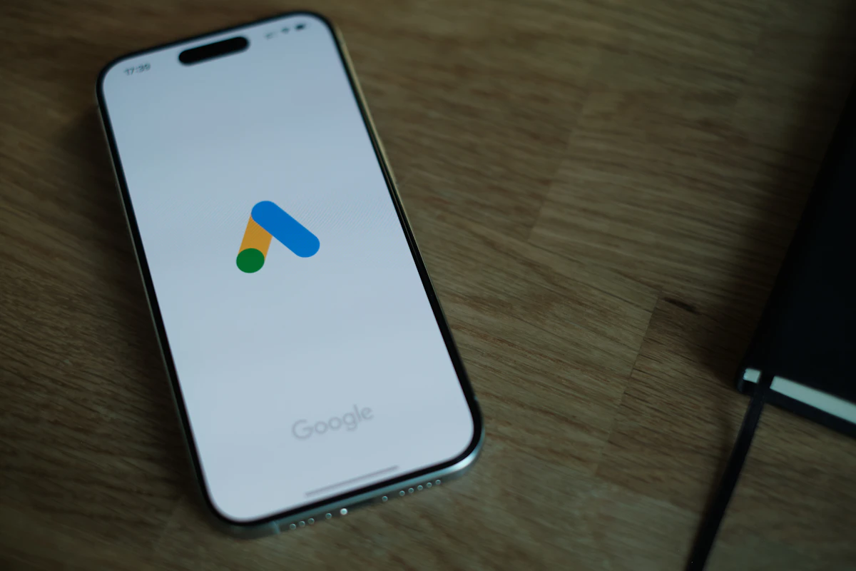Telemóvel pousado numa secretária de madeira com o logótipo do Google Ads no ecrã