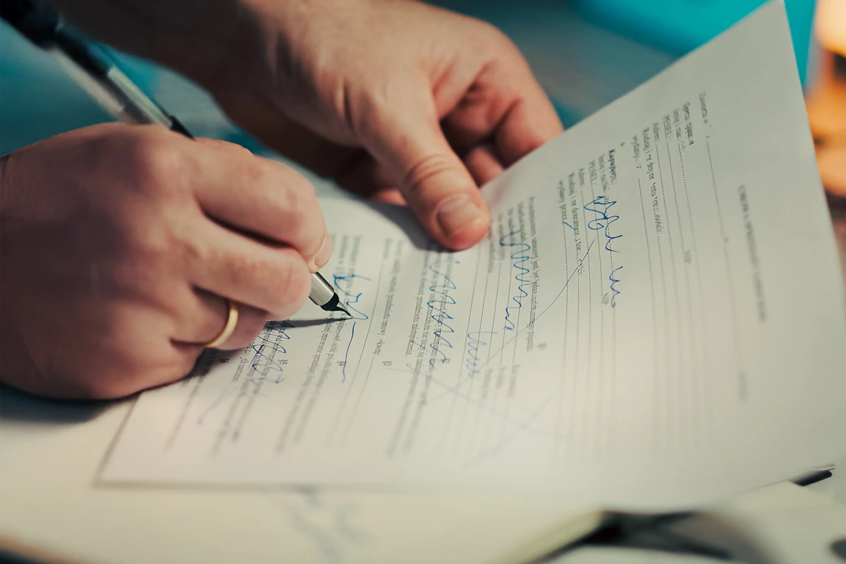Mão a assinar um documento com uma caneta