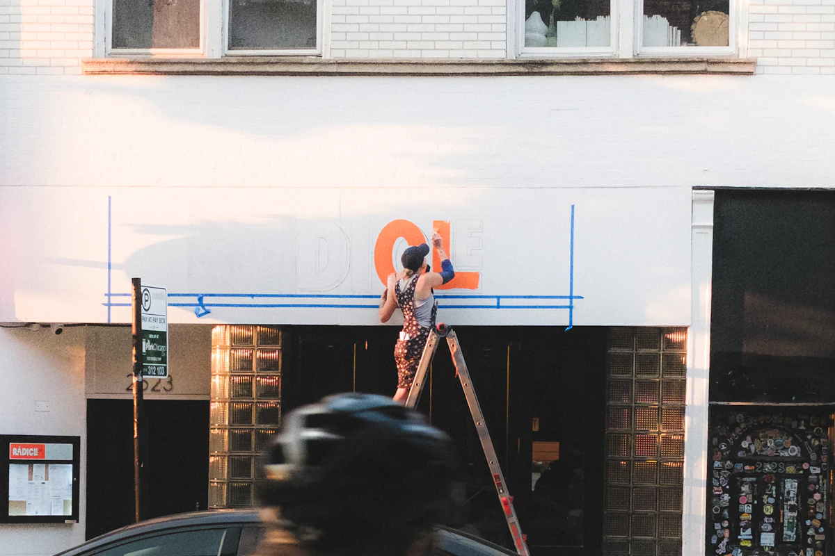 Fachada de um edifício com um trabalhador numa escada a instalar letras grandes de um letreiro novo