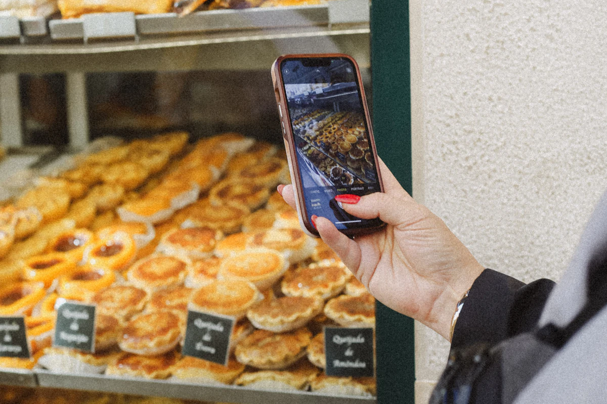 Mão a filmar com o telemóvel uma montra de pastéis de nata numa pastelaria
